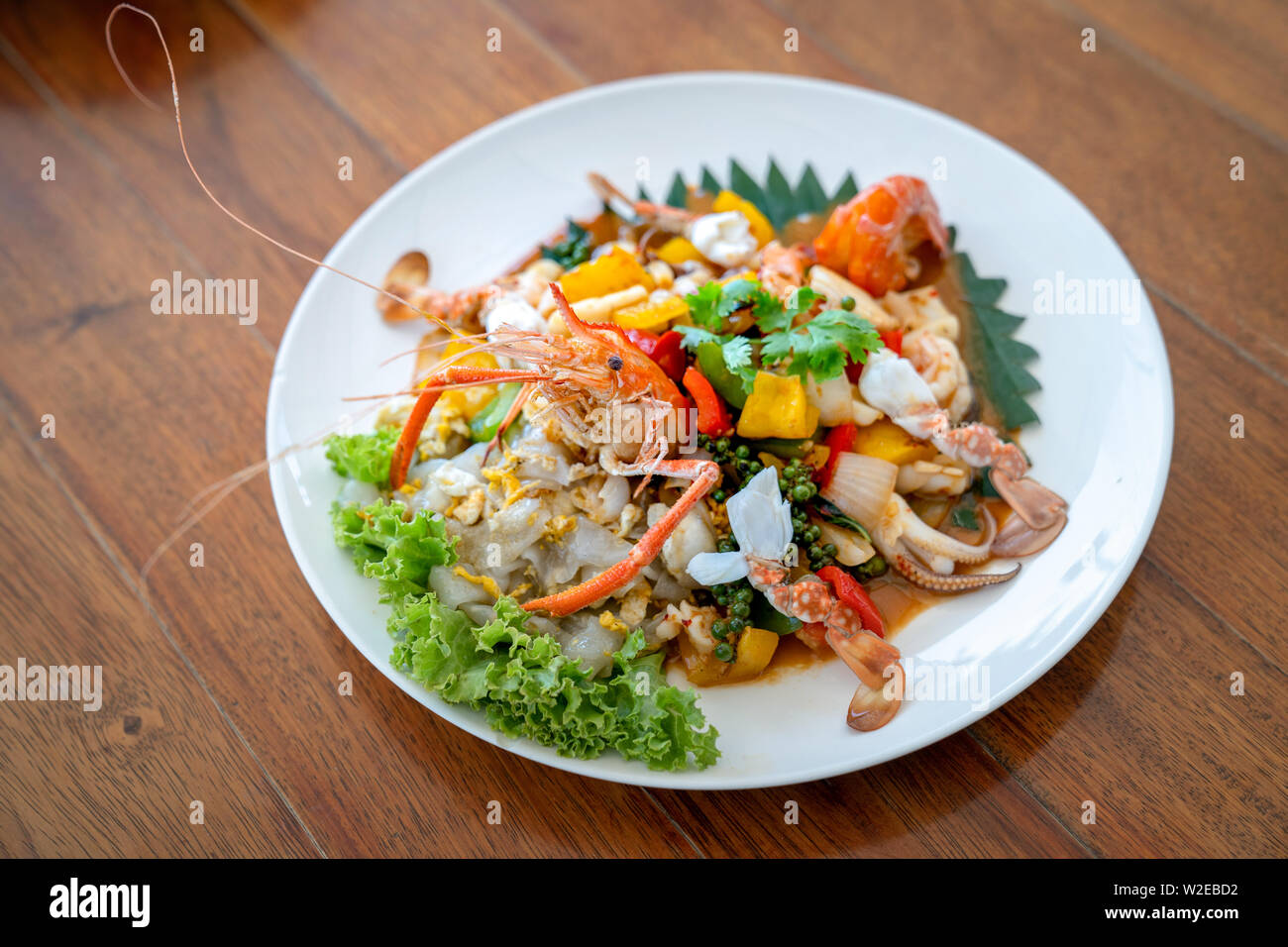 Seafood Thai mixxed together between boiled shrimp, crab, squid and colourful vegetable in dish on wood table in restaurant. Stock Photo