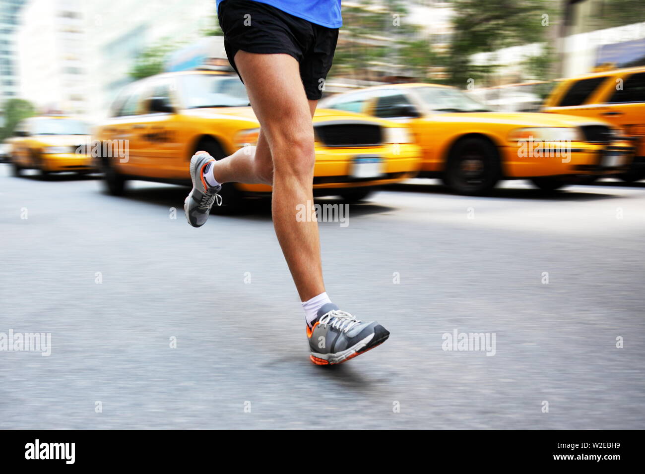 Running in New York City - man city runner jogging in street of Manhattan with yellow taxi caps cars and traffic. Urban lifestyle image of male jogger training downtown. Legs and running shoes. Stock Photo