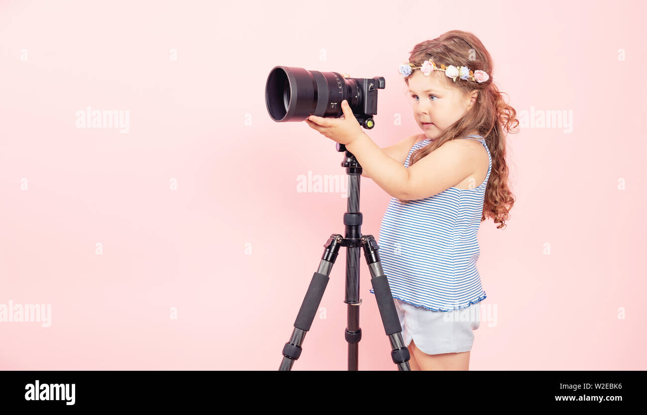 Little girl holding camera and smiling on pink background. Stock Photo