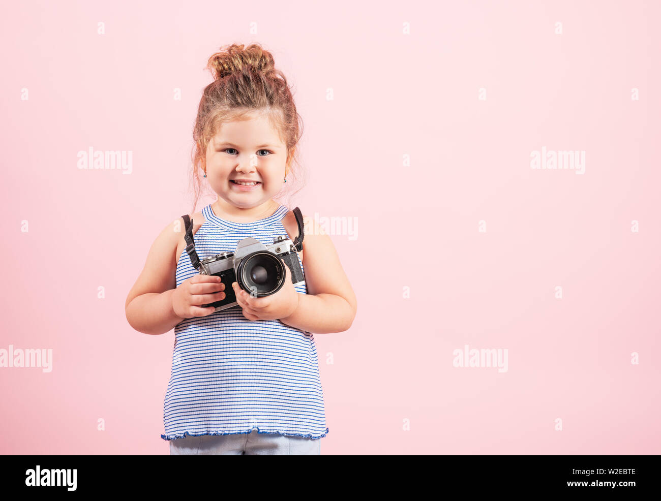 Little girl holding old vintage camera and smiling on pink background. Stock Photo