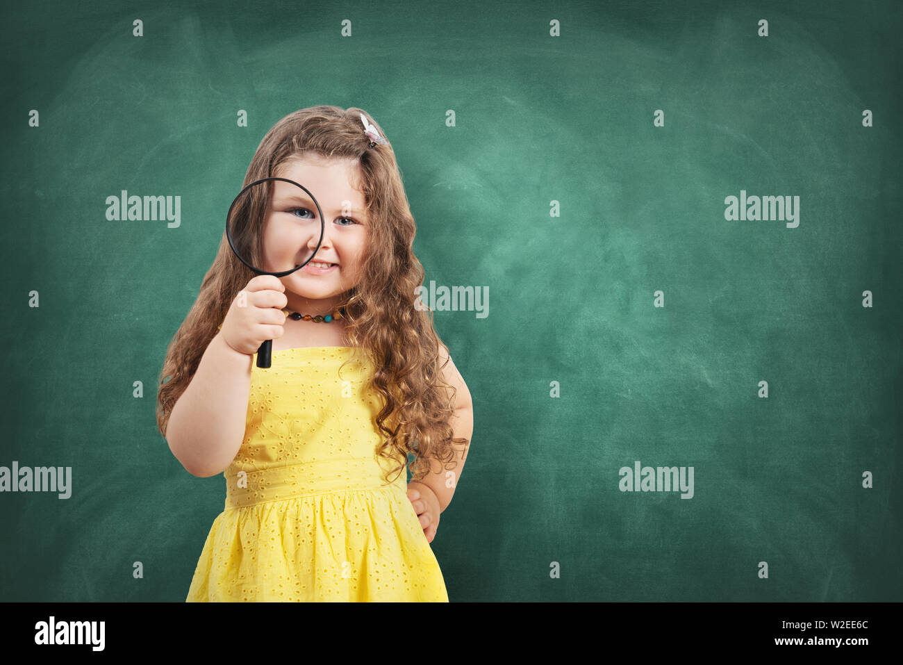 Little curious school girl with magnifier on chalkboard. Stock Photo