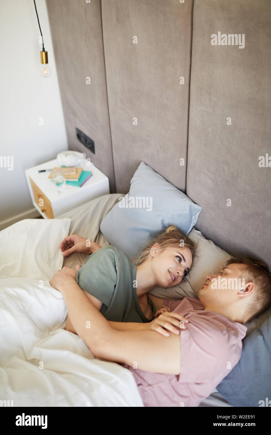 Happy young amorous spouses looking at one another while lying in bed Stock Photo