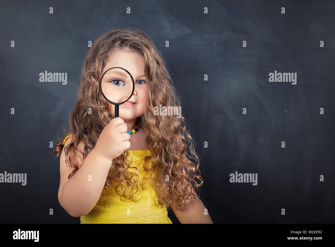 Little curious school girl with magnifier on chalkboard. Stock Photo