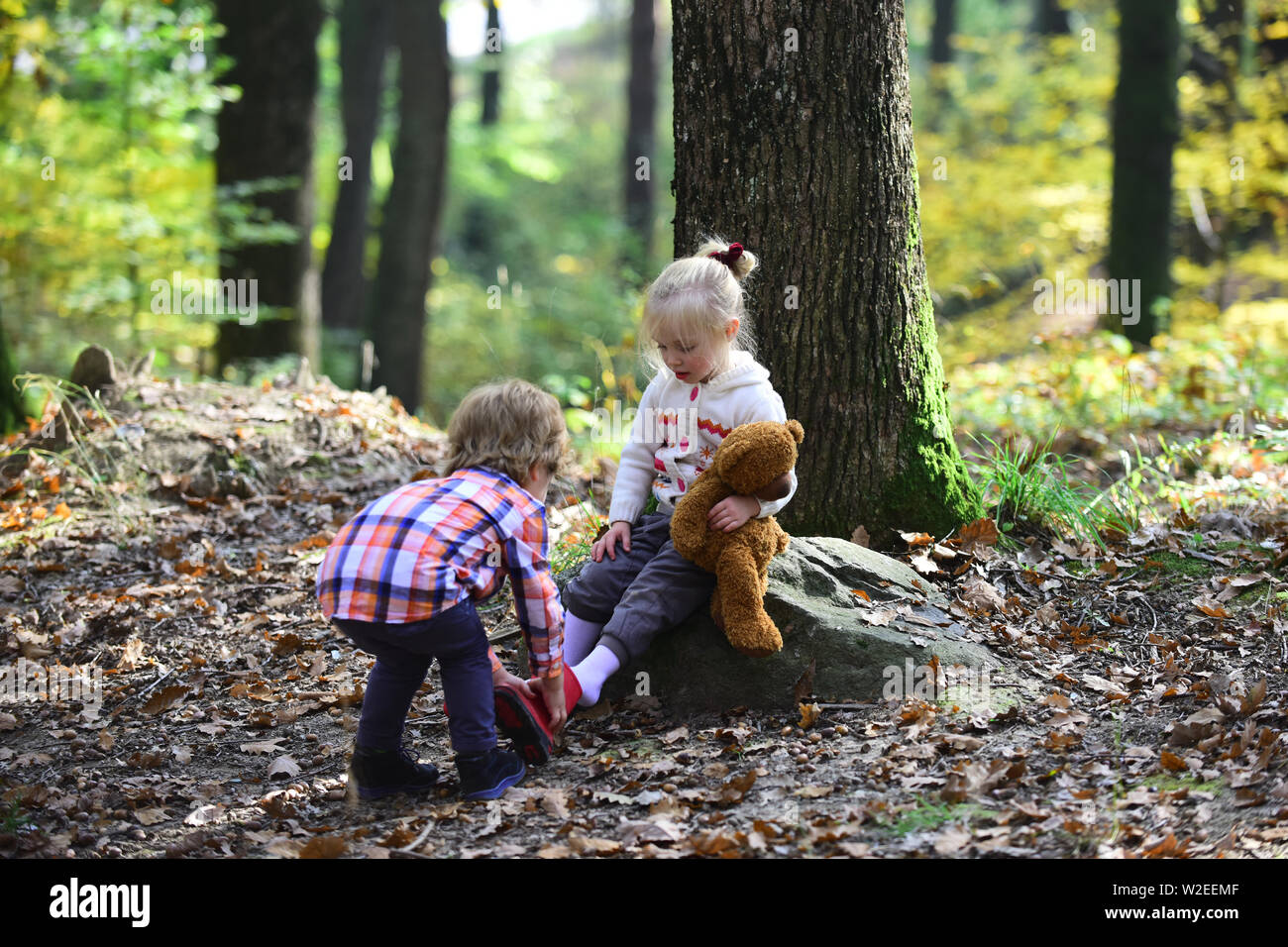 Little boy put shoes on girl feet. Brother help sister to put red boots