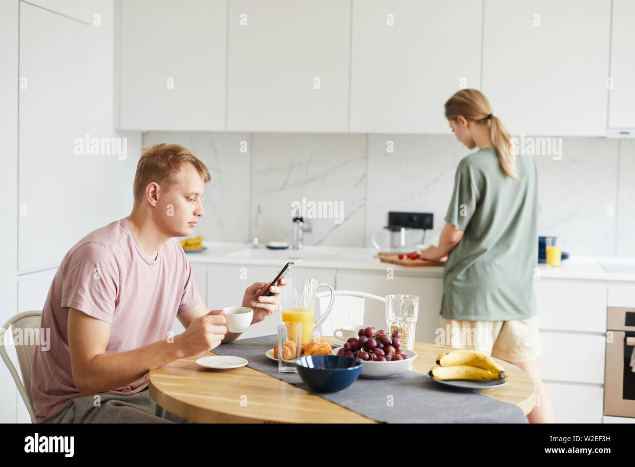 Young man with smartphone having coffee by served table while scrolling in gadget Stock Photo
