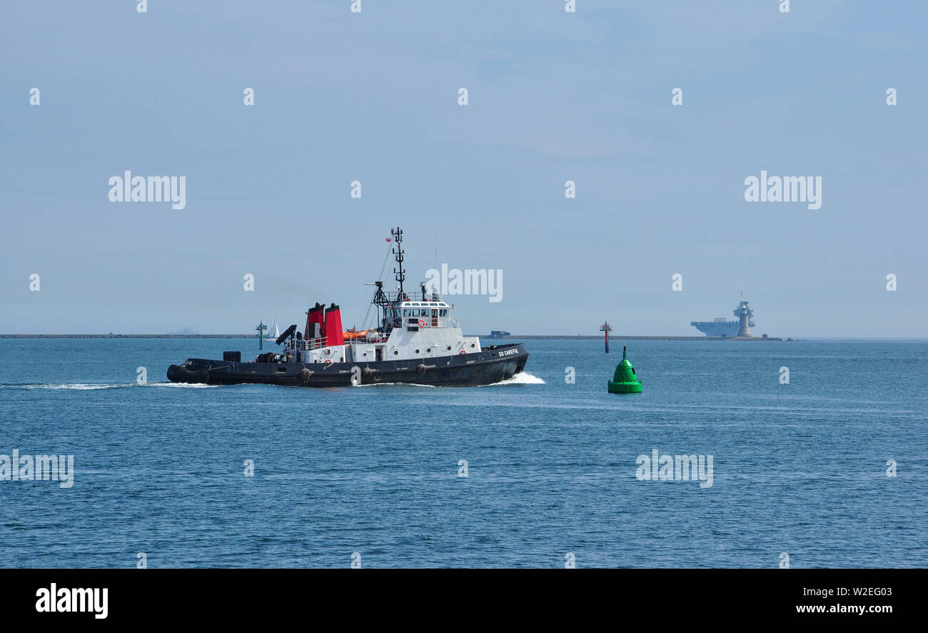 Twin Unit Tractor Tug, SD Careful, in Plymouth Sound with Aircraft Carrier HMS Queen Elizabeth beyond the breakwater, Devon, England, UK Stock Photo