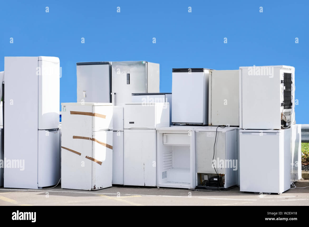 Old fridges freezers refrigerant gas at refuse dump skip recycle stacked pile help environment reduce pollution white silver blue sky Stock Photo