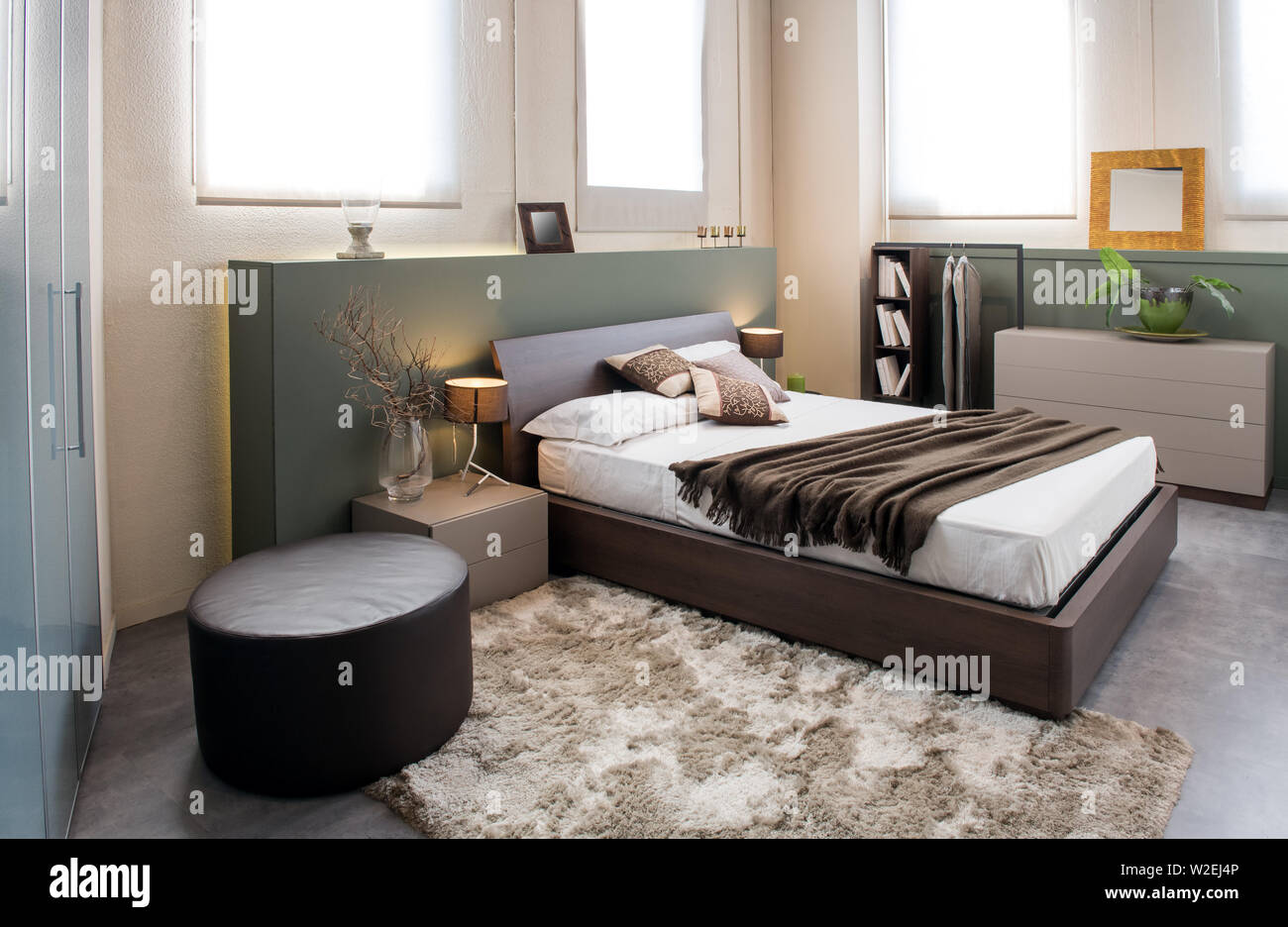 Modern luxury brown monochrome bedroom interior with large headboard above a double beds with cabinets, ottoman and built in wardrobe Stock Photo