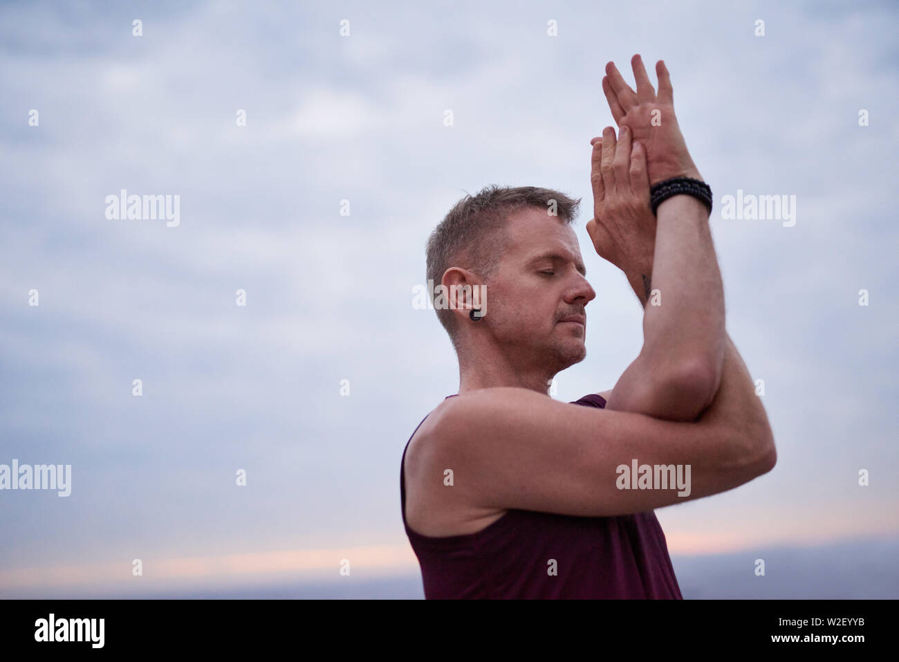 Man doing the eagle pose by the oceanat dusk Stock Photo