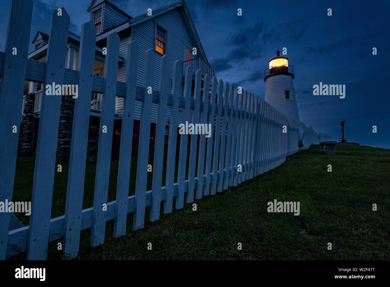 The historic Pemaquid Point Lighthouse, keepers cottage and white picket fence at twilight in Bristol, Maine. The picturesque lighthouse built along the rocky coast of Pemaquid Point was commissioned in 1827 by President John Quincy Adams. Stock Photo