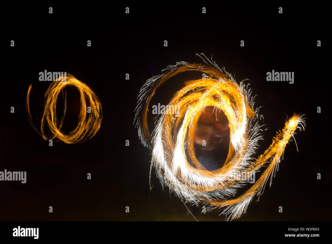 An artist shows a fire show at night spinning torches, circles of fire ...