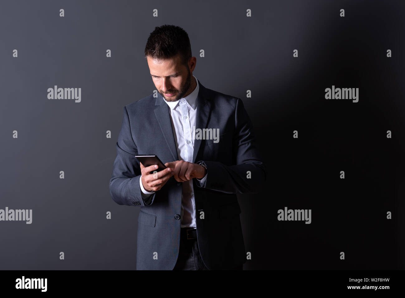 A serious handsome young businessman in a suit using his smartphone in ...