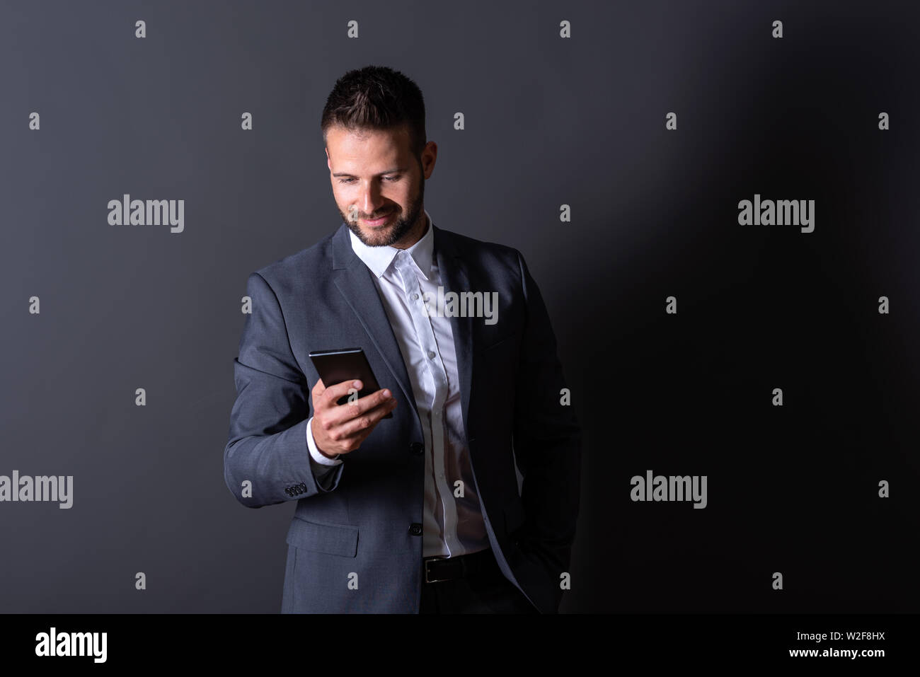 A smiling handsome young businessman in a suit using his smartphone in ...