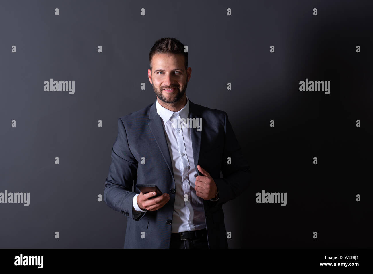 A smiling handsome young businessman in a suit using his smartphone in ...