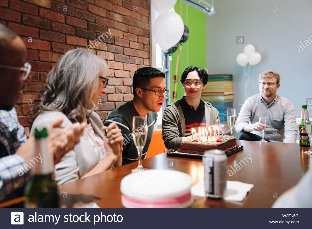 Business people watching colleague blow out birthday cake candles in