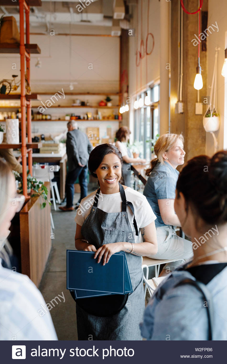 Smiling hostess with menus greeting customers in restaurant Stock Photo