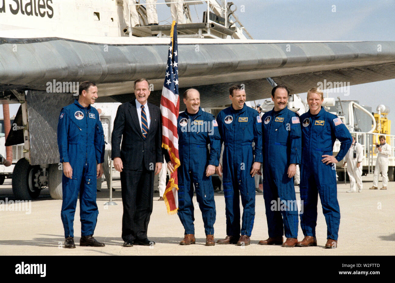 (3 Oct 1988) --- The five STS 26 crewmembers pose with Vice President George Bush after completing a successful four-day mission aboard the Space Shuttle Discovery (background). Pictured, from left to right, are  astronaut Richard O. Covey, pilot; Vice President Bush; and astronauts Frederick H. (Rick) Hauck, mission commander;  and David C. Hilmers, John M. (Mike) Lounge,  and George D. Nelson, all mission specialists. Stock Photo