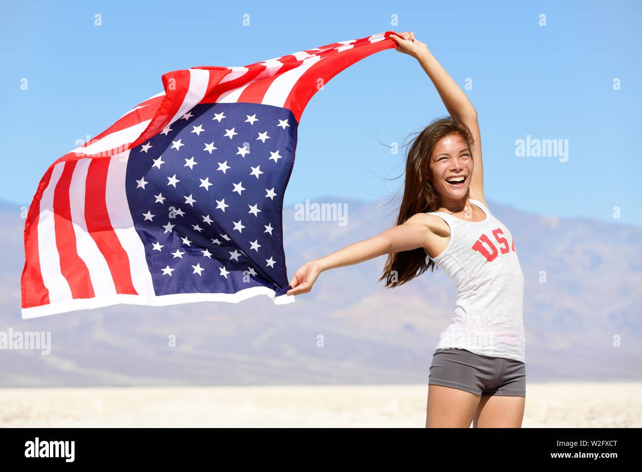 American flag - woman USA sport athlete winner cheering waving stars and stripes outdoor after in desert nature. Beautiful cheering happy young multicultural girl joyful and excited. Stock Photo