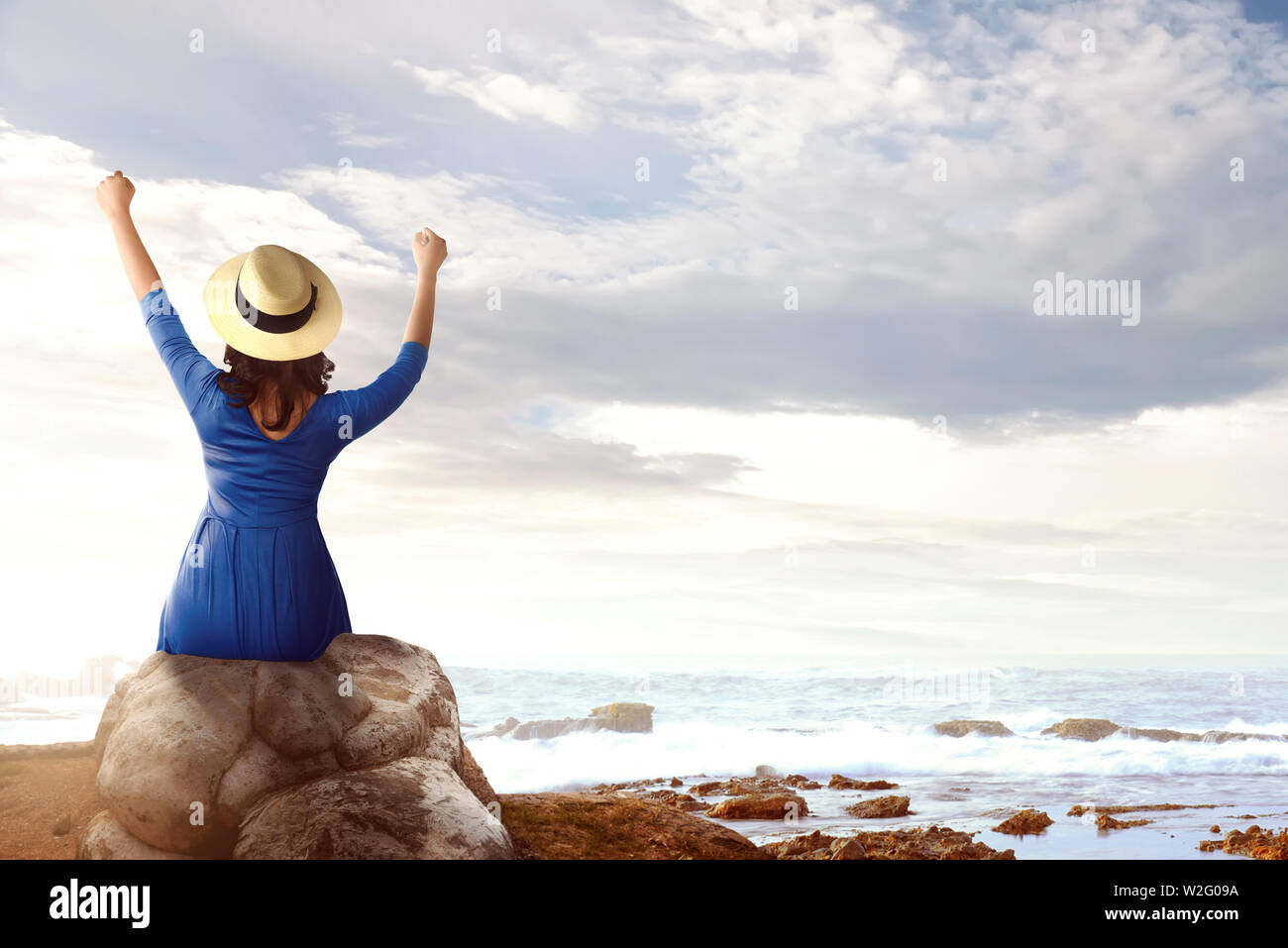 Rear view of asian woman in hat sitting on the rock and looking at the ...