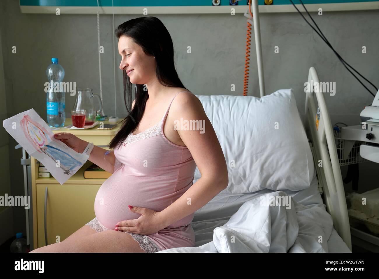Pregnant woman sitting on sickbed in hospital room with picture of child, high-risk pregnancy, Karlovy Vary, Czech Republic Stock Photo
