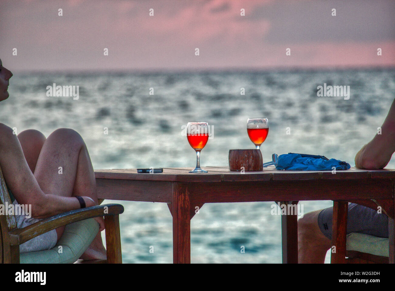 This unique image shows a couple at a romantic sunset. The two enjoy a drink. This photo was taken in the Maldives Stock Photo