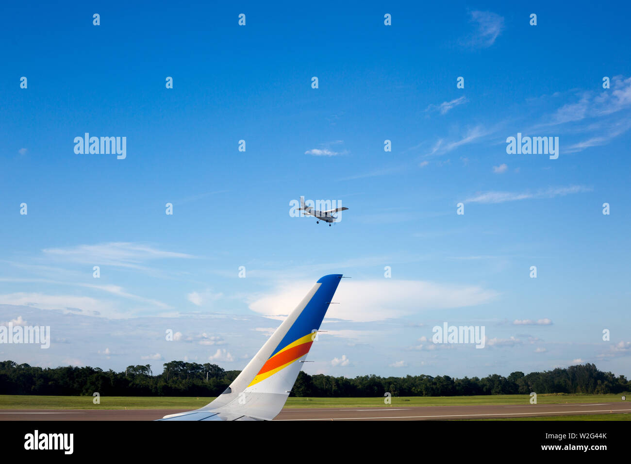 A small plane lands just beyond the wingtip of an Allegiant Airbus A320 jet airliner at Orlando Sanford International Airport in Sanford, Florida, USA. Stock Photo