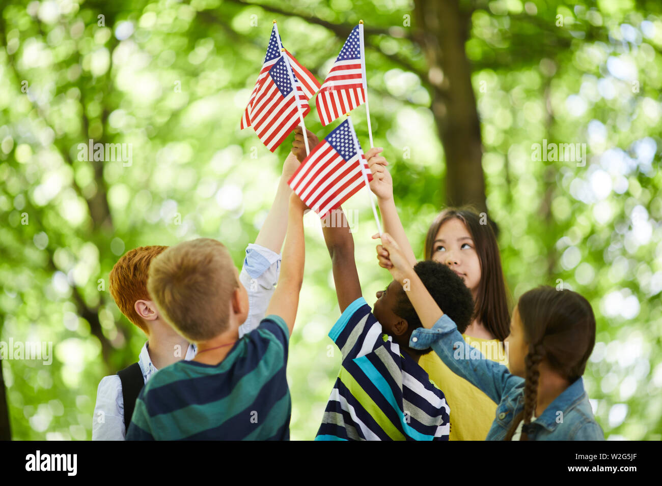 Group of patriotic multi-ethnic children standing in circle and raising us stick flags together Stock Photo