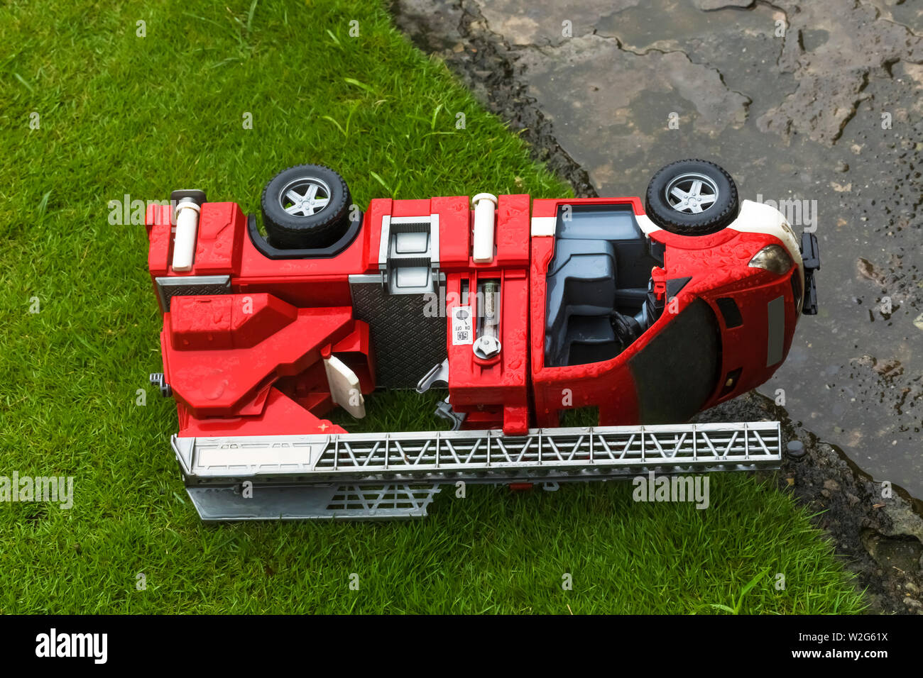 Toy fire engine abandoned on the grass lone in the rain. Stock Photo