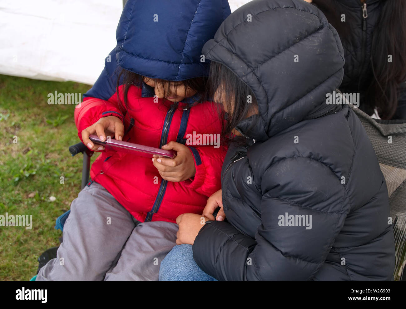 Meriden, CT USA. Apr 2019. Daffodil Festival. Native American children huddled together playing online games on their phone. Stock Photo