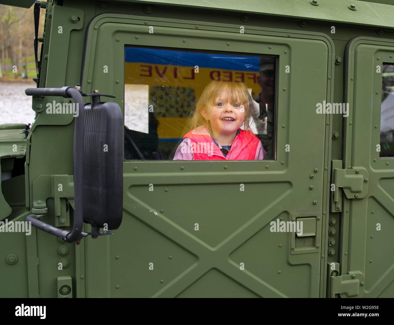 Meriden, CT USA. Apr 2019. Daffodil Festival. Young girl inside a military Humvee smiling at soldier dad. Stock Photo