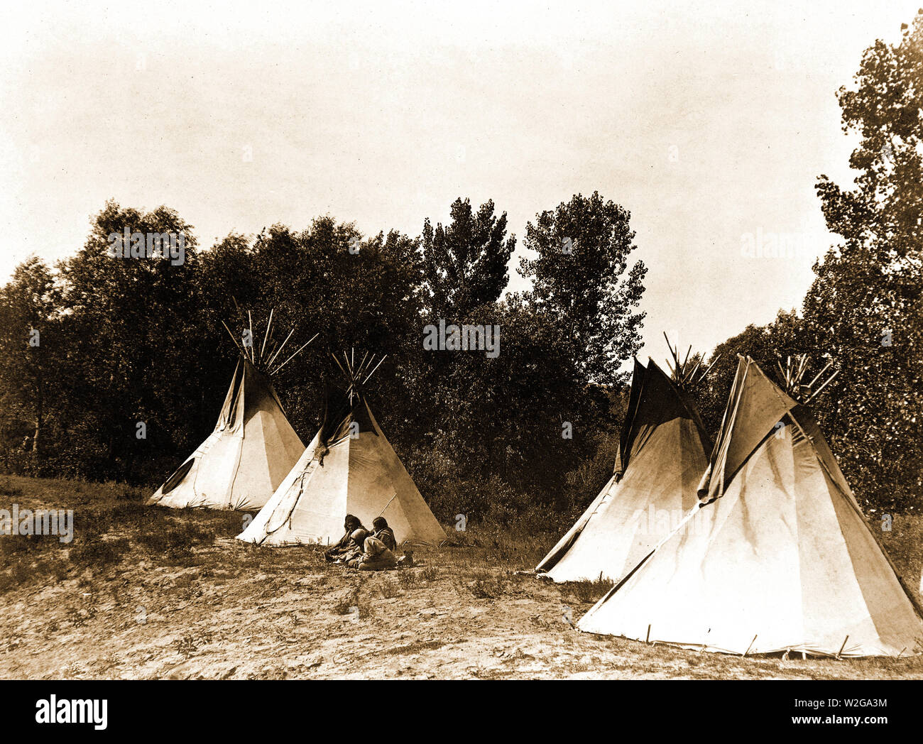 Edward S. Curtis Native American Indians - An Assiniboin camp containing four tepees with Indians seated on ground ca. 1908 Stock Photo
