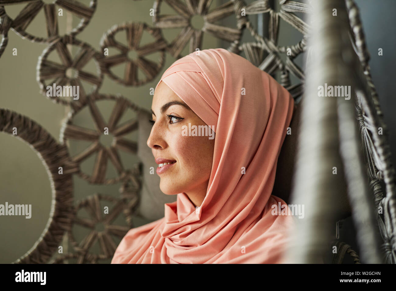 Pretty smiling pensive young woman with freckles wearing light pink hijab Stock Photo