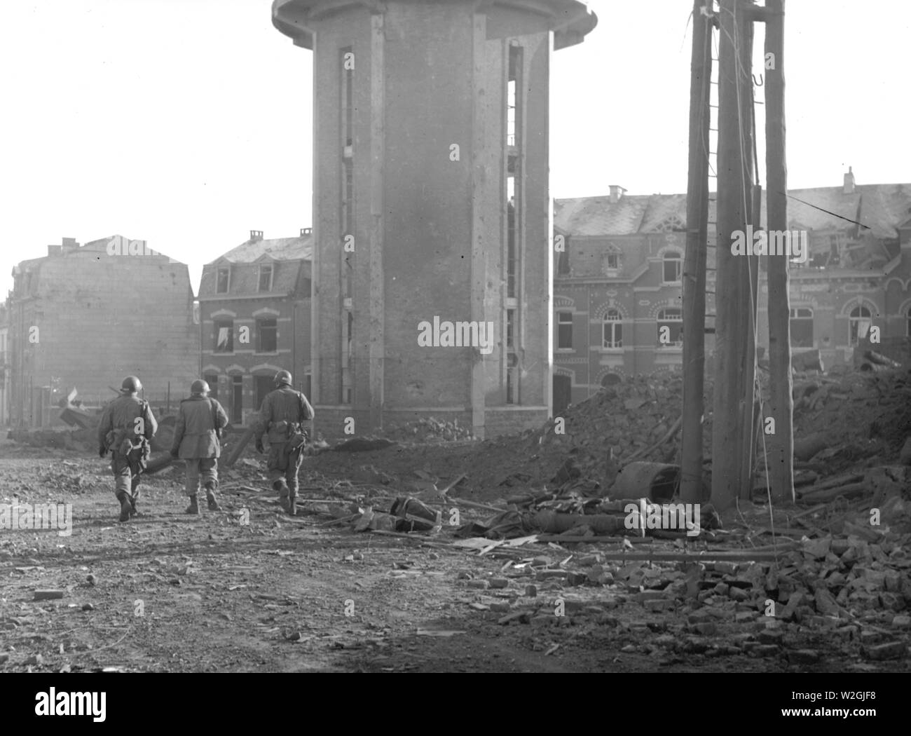 Original caption: Members of the 101st Airborne Division walk past dead comrades, killed during the Christmas Eve bombing of Bastogne, Belgium, the town in which this division was besieged for ten days. This photo was taken on Christmas Day. 1944 Stock Photo