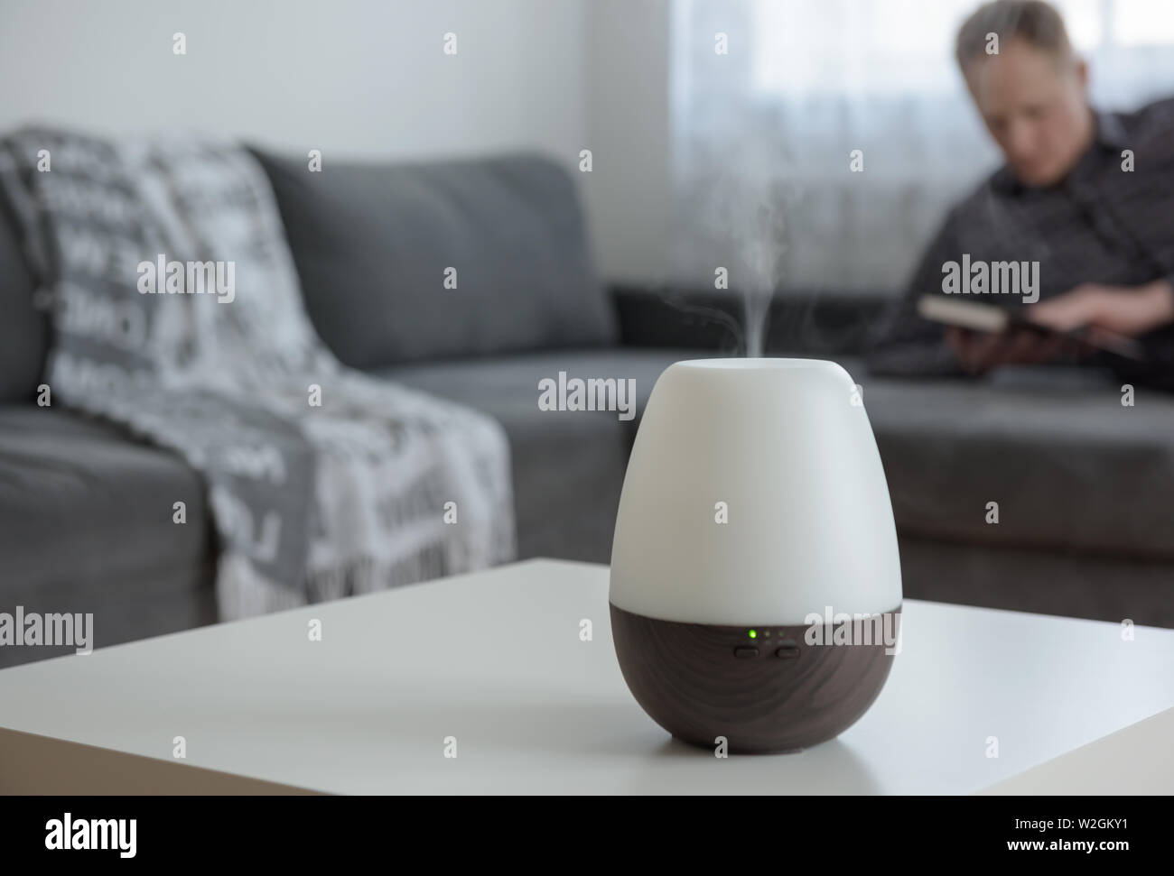 Aromo diffuser on a white table on the background of the interior. In the background, a man is reading a book. Stock Photo