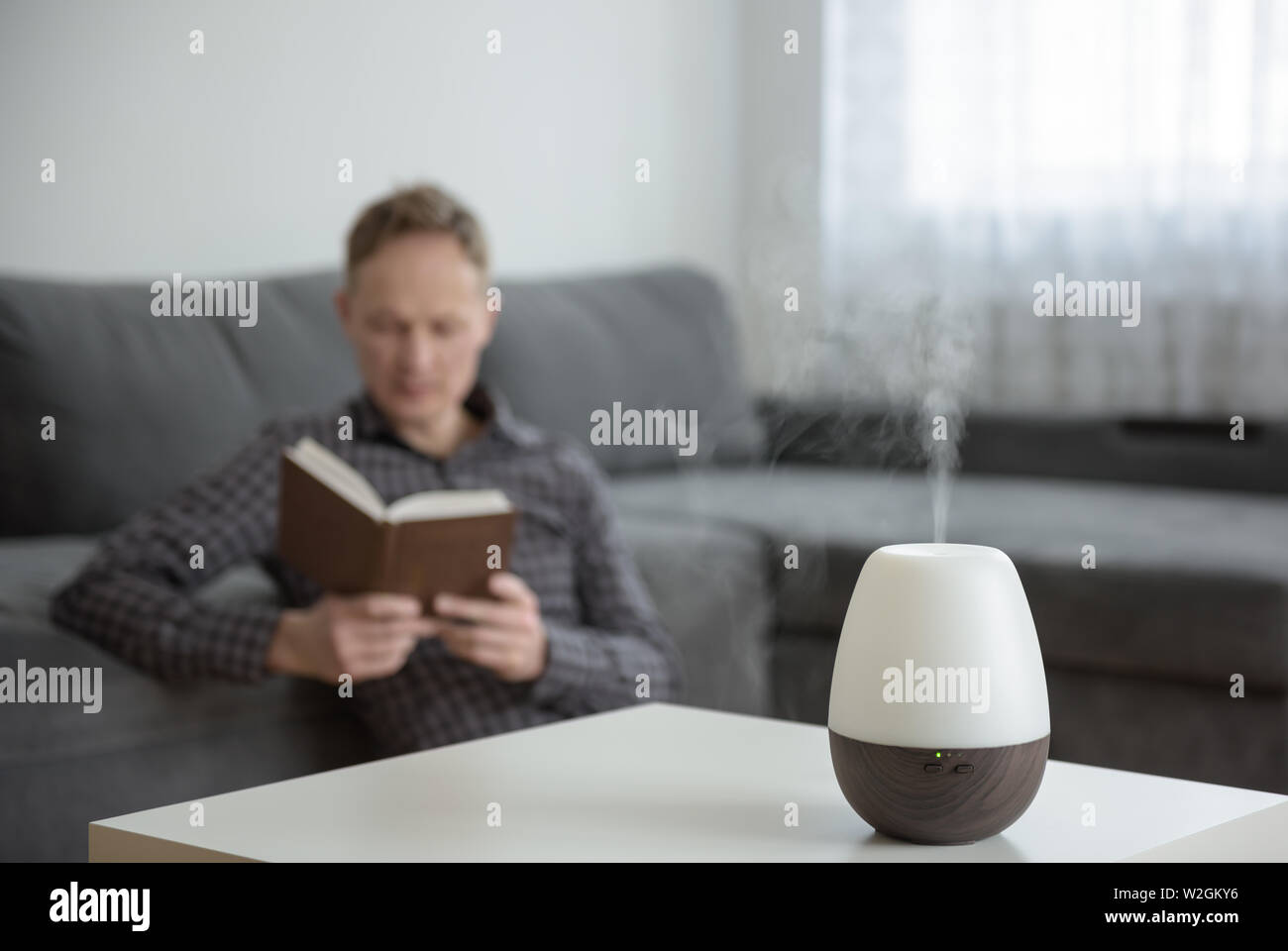 Aromo diffuser on a white table on the background of the interior. In the background, a man is reading a book. Stock Photo