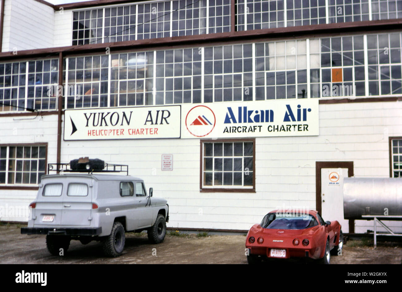 Cars parked at an airport in Alaska outside the offices of Yukon Air and Alkan Air ca. 1983 Stock Photo