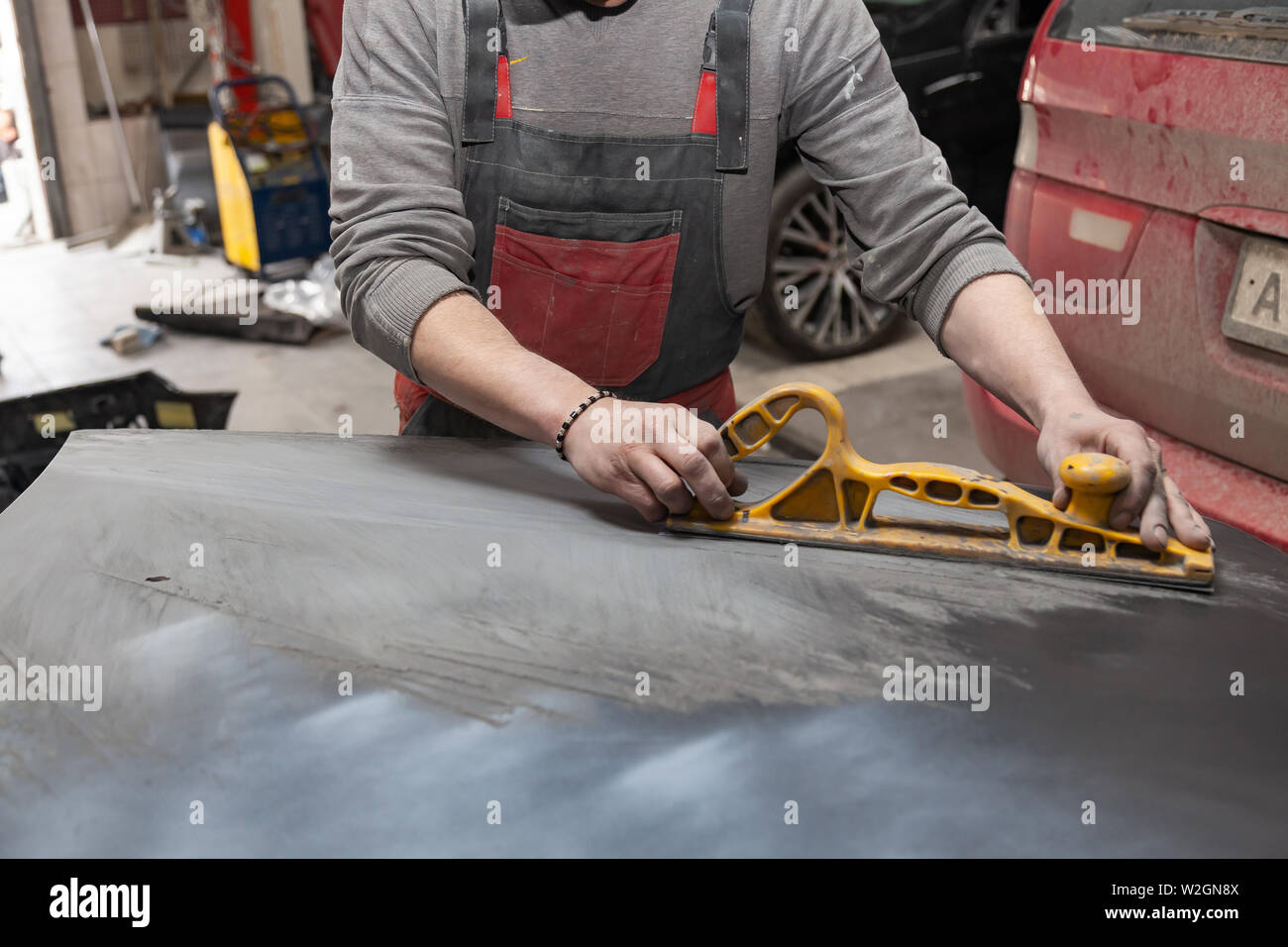 Man worker preparing for painting a car element using emery sender by a service technician