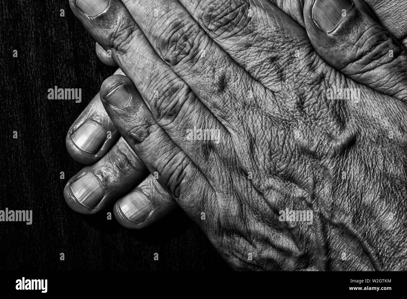 Black and White photo of senior man crossed hands detail on dark background Stock Photo