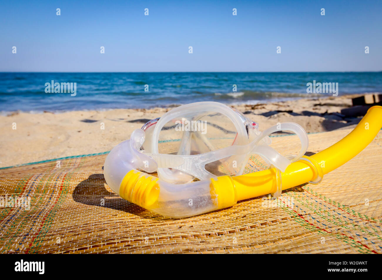 Diving mask and snorkel breather tube are placed on mat at the sandy beach. Stock Photo