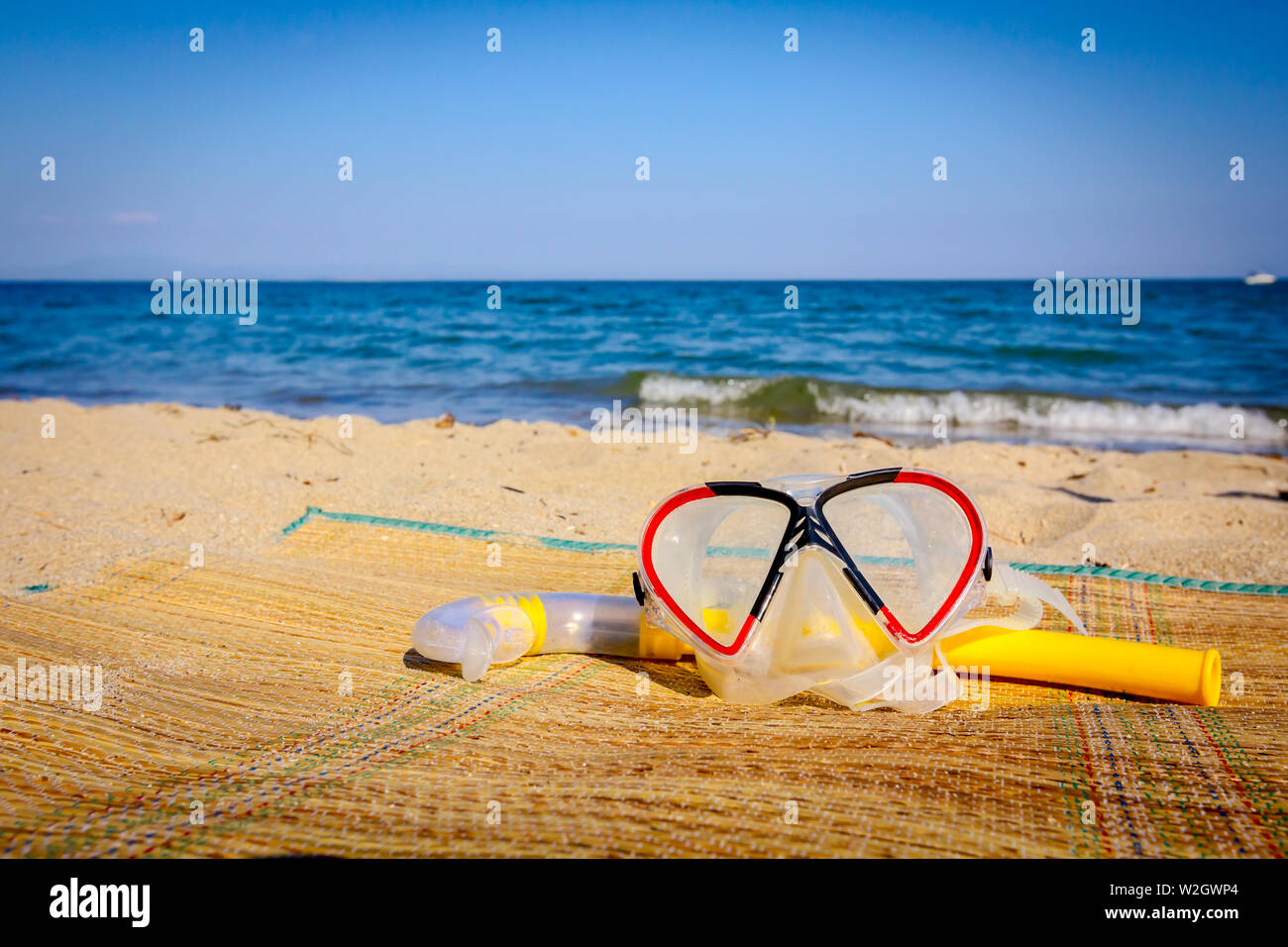 Diving mask and snorkel breather tube are placed on mat at the sandy