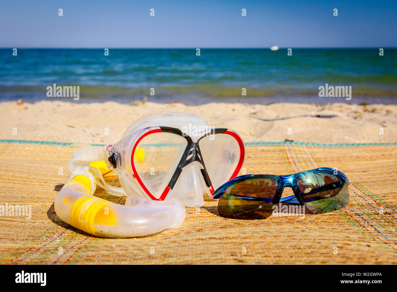 Diving mask, snorkel breather tube and sun glasses are placed on mat at
