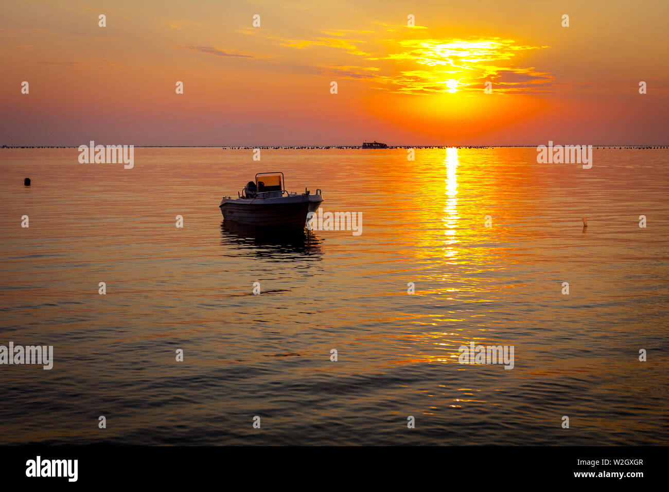 Silhouetted shot of beautiful sunrise with fisherman boat on the water ...