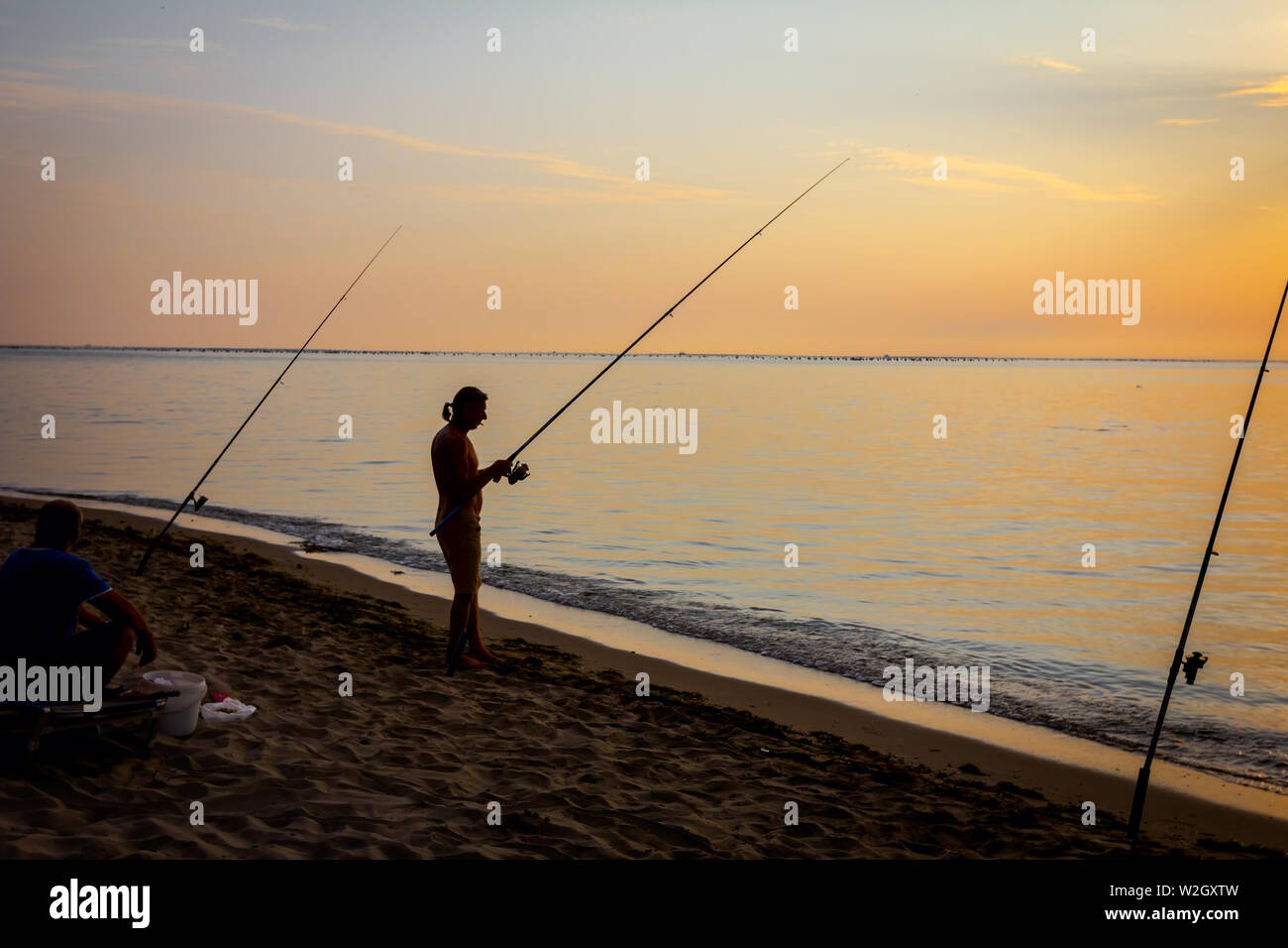 https://c8.alamy.com/comp/W2GXTW/two-buddies-are-catching-fish-from-the-sandy-beach-with-fishing-rods-sunrise-morning-over-mediterranean-sea-W2GXTW.jpg