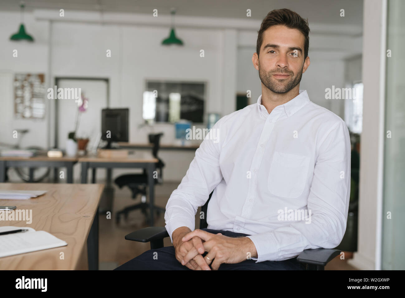 Confident young businessman sitting alone in a large modern office Stock Photo