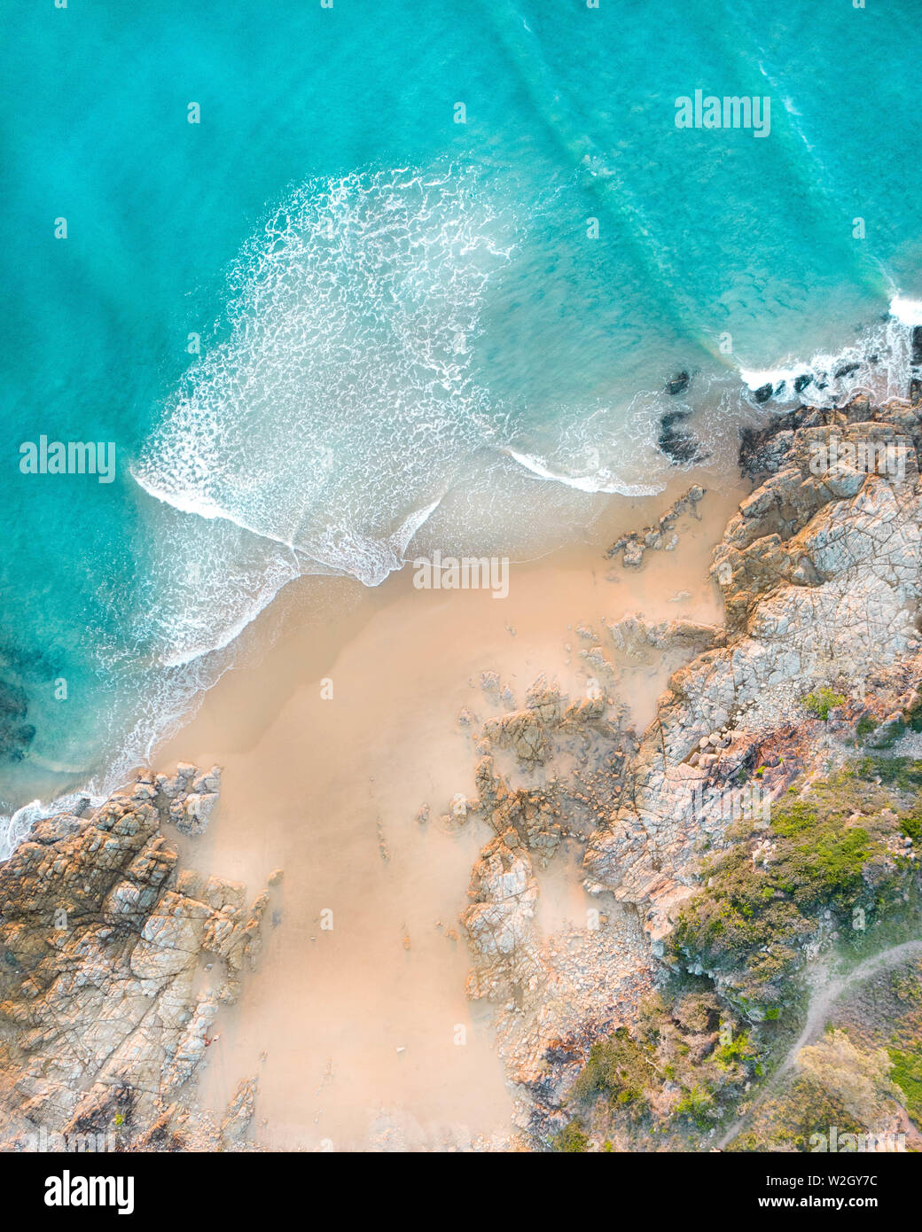Aerial of a beach with beautiful waves, white sand and rocks at sunset in Australia Stock Photo