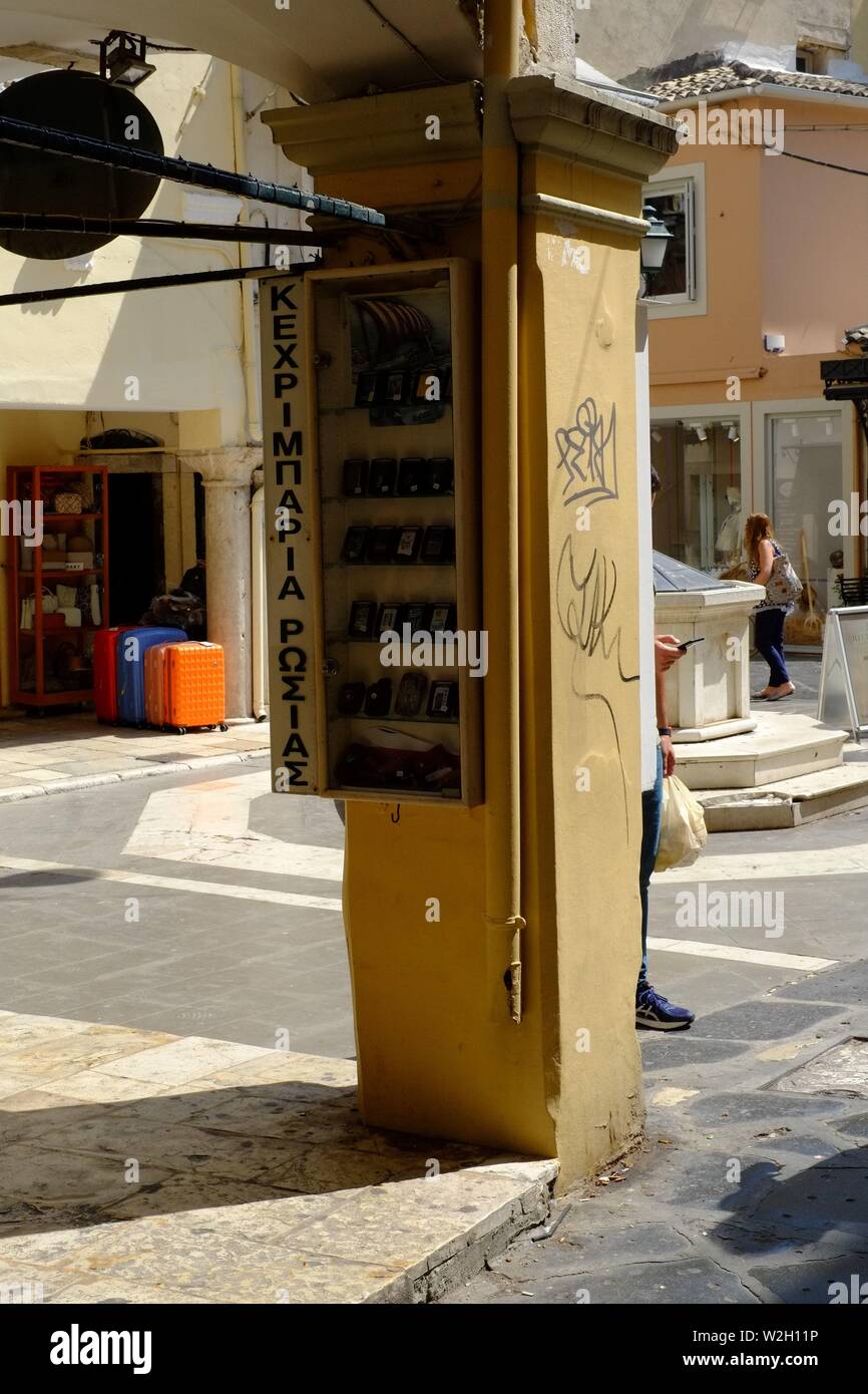 Corfu town scene central in a square with shops around not many people a central pillar with a sign on is the main point of interset Stock Photo