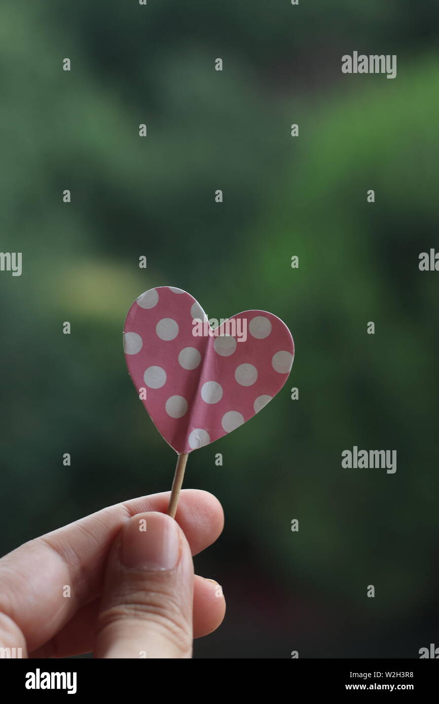 Hand holding pink polka dot paper heart Stock Photo