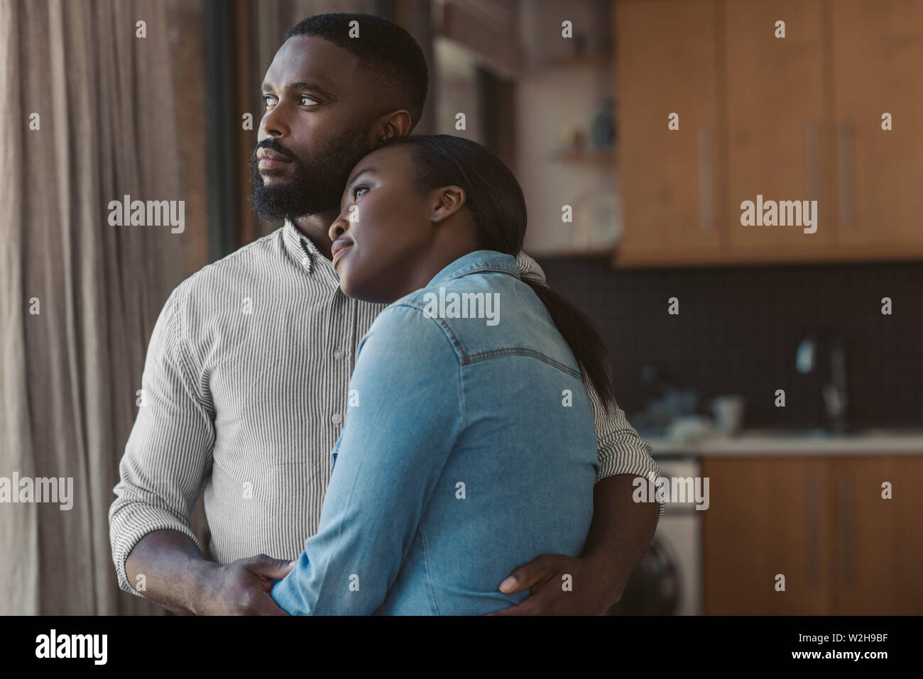African American couple hugging and looking out of their window Stock Photo