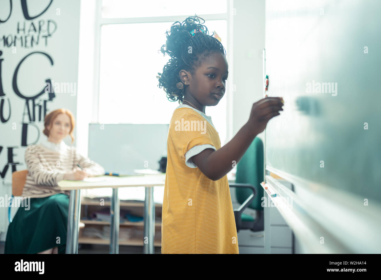 Thoughtful girl going to write on a blackboard. Stock Photo