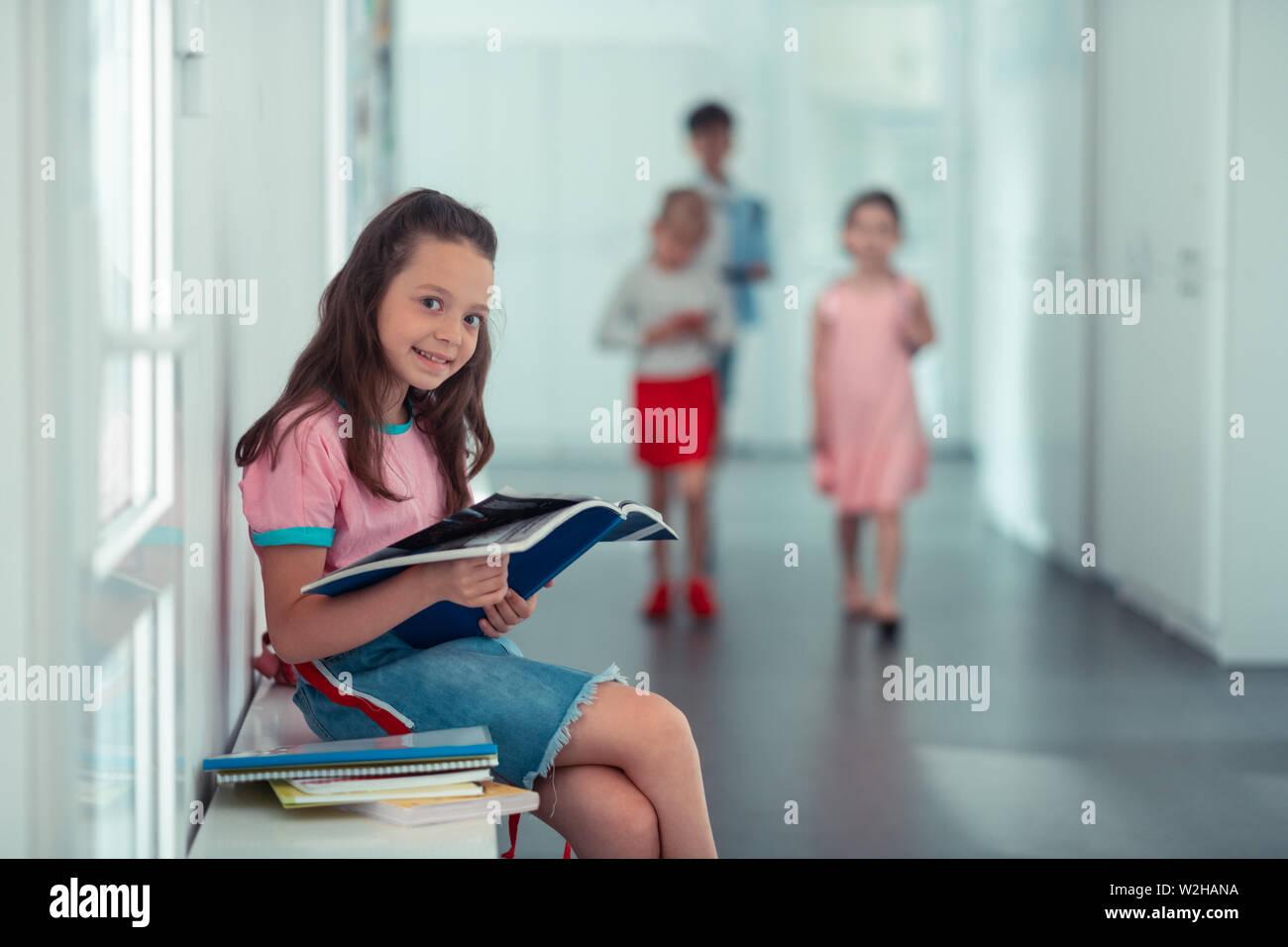 Girl smiling while sitting near window and reading book Stock Photo - Alamy
